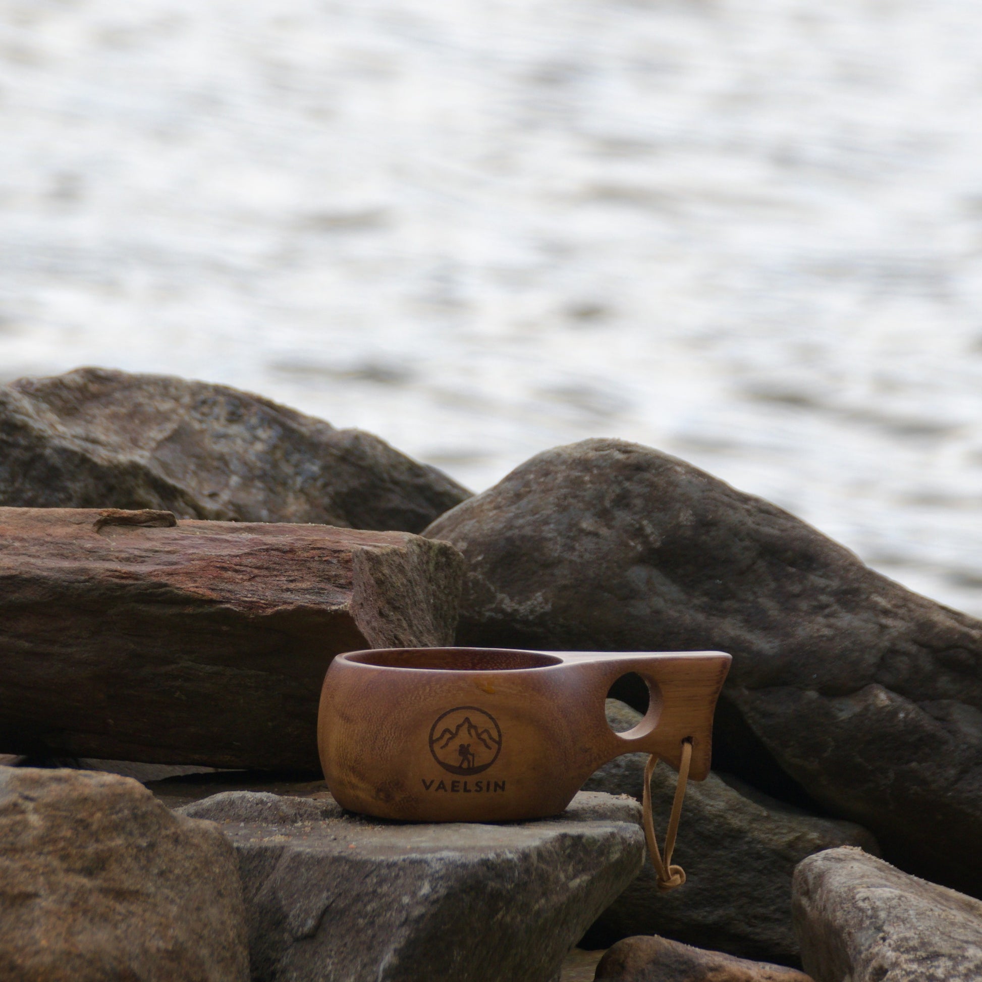 Wooden cup with a handle on rocks by the water.